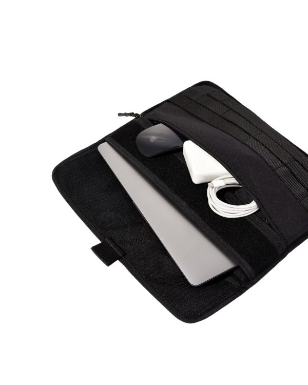 Angled top view of the black SYMA Command demonstrating its storage capacity, with a silver MacBook partially inserted and its front pocket holding a mouse, charger, and cable. Tactical laptop sleeve.