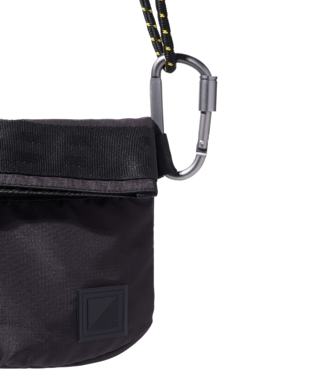 Close-up view of the black SYMA Chain highlighting its subtle rubberized logo patch, fabric texture, and silver carabiner hardware. Compact sacoche bag.
