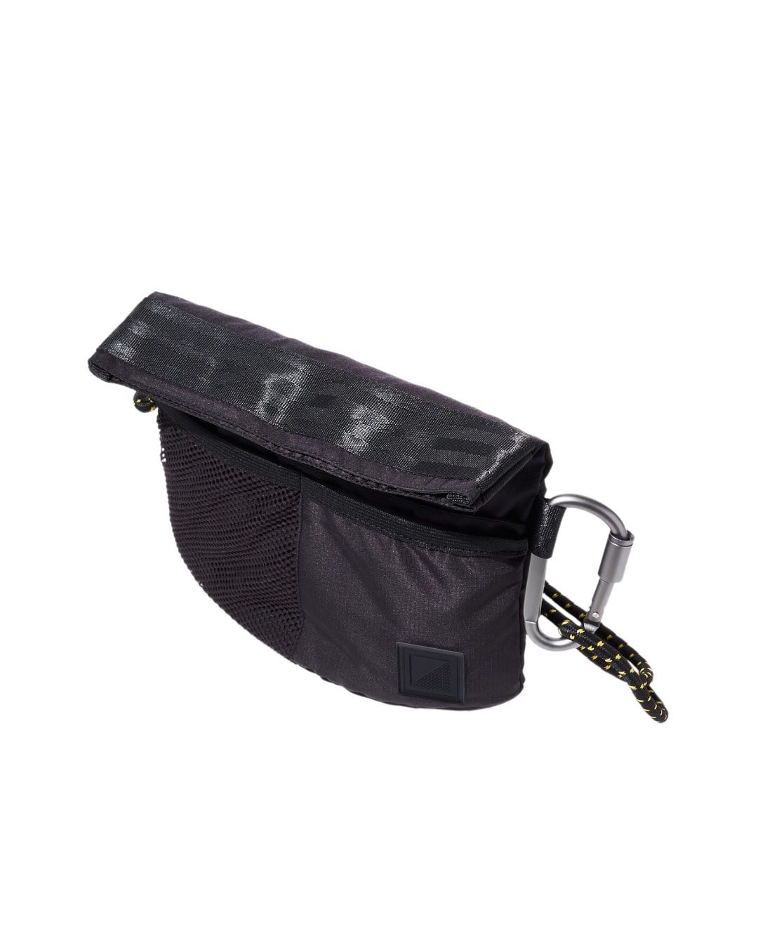 Angled top view of the black SYMA Chain highlighting its textured fold-over flap, half-mesh front pocket, and silver carabiner. Compact sacoche bag.