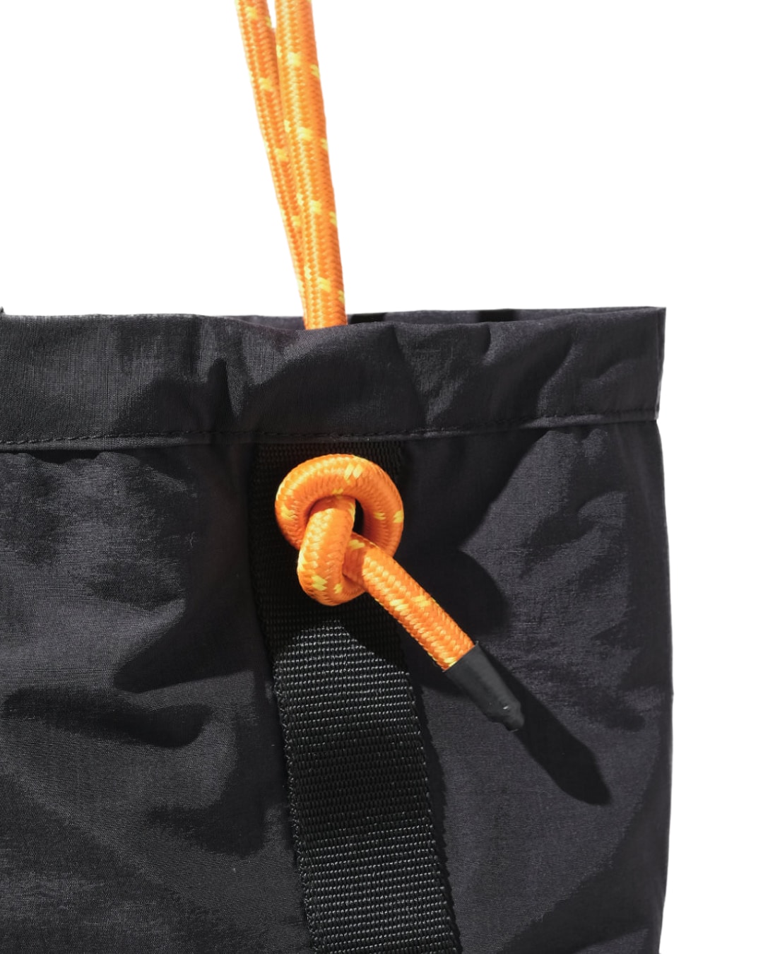 Close-up detail of the black SYMA Noble minimalist everyday tote bag, highlighting the textured nylon crinkle fabric, sturdy 2.5cm webbing, and the knotted orange paracord strap