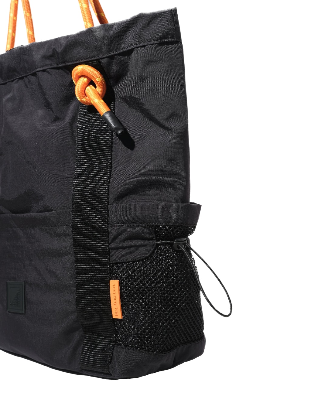 Close-up side view of the black SYMA Noble minimalist everyday tote bag, highlighting the exterior mesh water bottle pocket, 2.5cm webbing, and textured nylon crinkle fabric