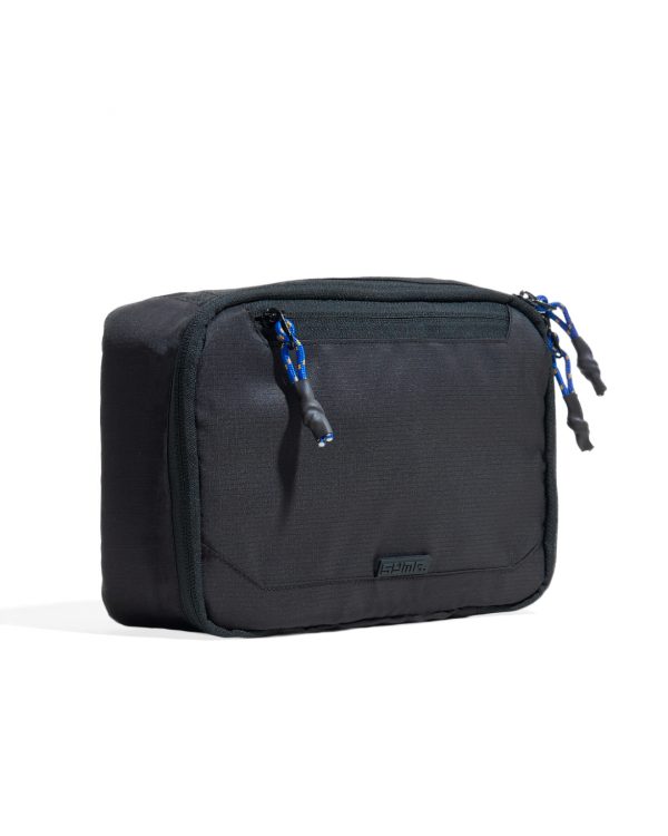 Closed three-quarter perspective view of the SYMA Refine Toiletry Kit in black, showcasing its water-resistant nylon exterior, quick-access front zipper pocket with blue paracord puller, main dual-zipper closure, and embossed black SYMA logo tag