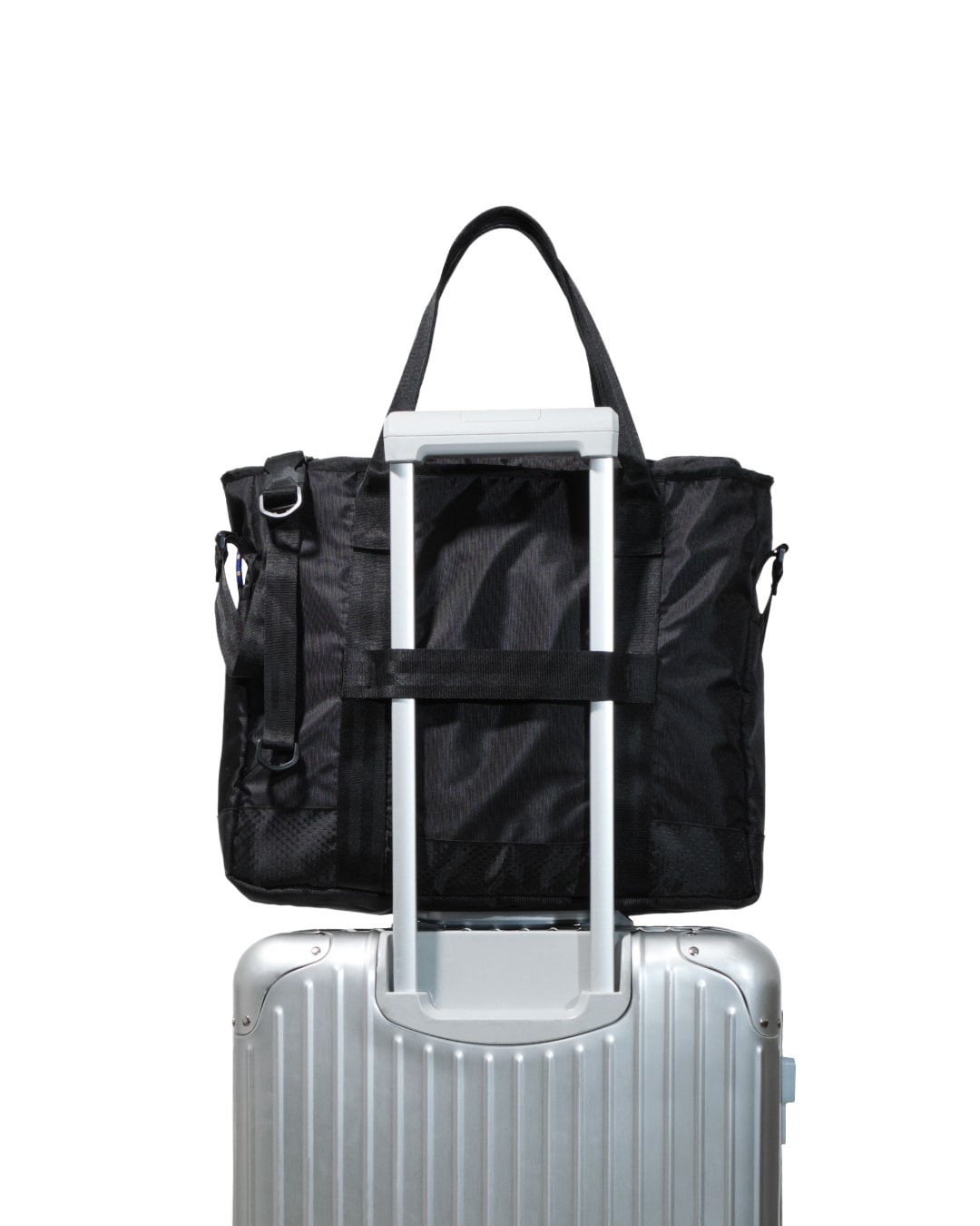 Rear view of black SYMA Miles Tote Bag attached to silver luggage handle using its slip-through strap. Versatile work tote bag