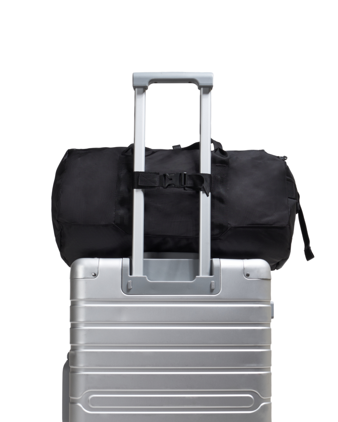 Demonstration of black SYMA Wonder Duffle Bag attached to silver suitcase handle using luggage strap. Versatile weekend duffle bag.