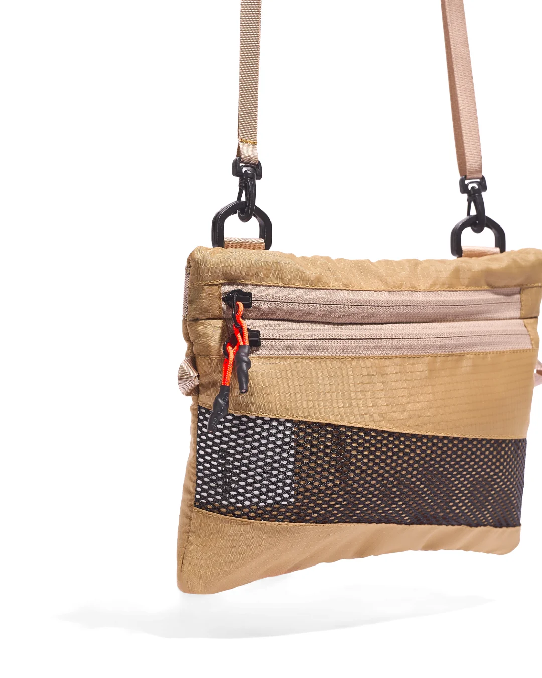 Close-up angled view of the SYMA Mantra khaki sacoche bag, highlighting the textured khaki 210D polyester ripstop fabric, dual front zippers with custom knotted orange and black paracord pullers, black bottom mesh panel, and black swivel carabiner hardware