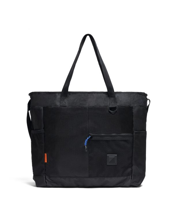 Straight front view of the SYMA Bridge Tote Bag in black, a premium urban utility tote featuring dual top handles, an adjustable crossbody strap, dual side mesh pockets, and a front compartment with a blue paracord YKK zipper puller